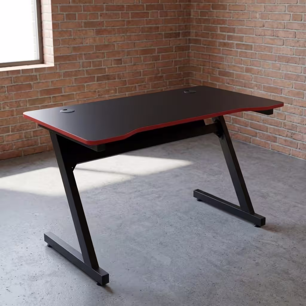 Ergonomic PC Gaming Desk featuring a matte black desktop with a curved front edge, a protective red trim, dual cable grommets, and a black steel Z-shaped leg frame.